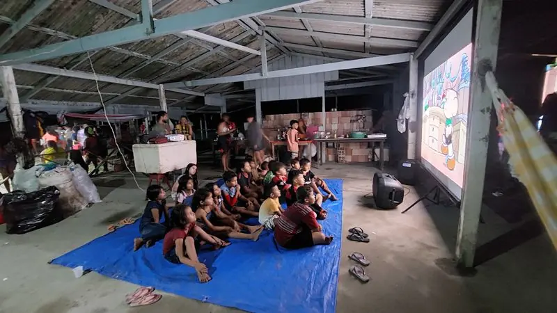 Crianças assistindo a um filme sobre uma lona azul